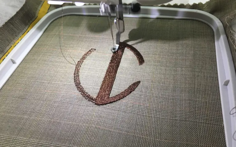 Close-up of a sewing machine embroidering the VC Wear logo onto fabric.