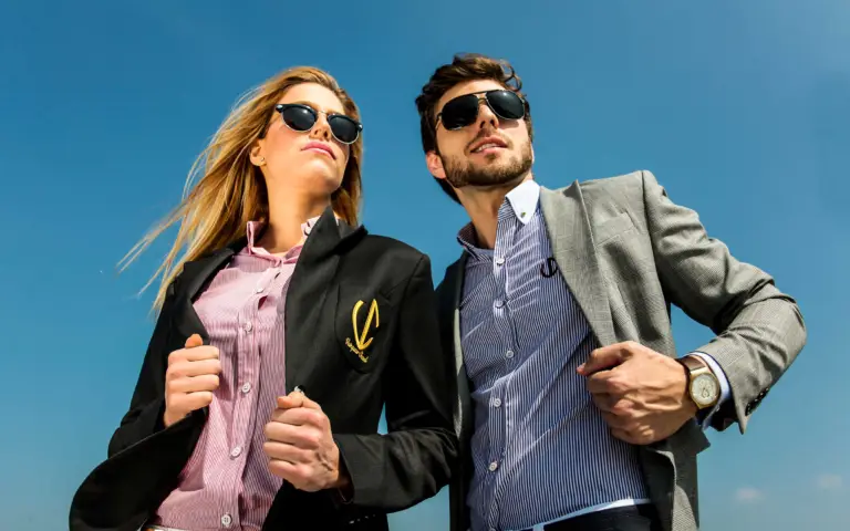 A man and a woman wearing stylish blazers and sunglasses, showcasing VC Wear apparel.