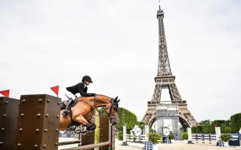 Equestrian rider in black jacket and white pants jumping a horse in front of the Eiffel Tower, showcasing VC Wear.